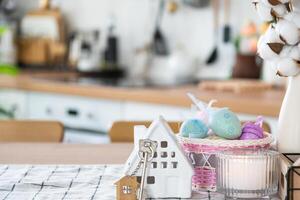 Key and tiny house of cozy home with Easter decor with color eggs on table of kitchen. Building, design, project, moving to new house, mortgage, insurance, rent and purchase real estate photo