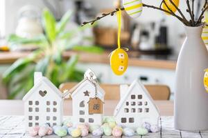 Key and tiny house of cozy home with Easter decor with color eggs on table of kitchen. Building, design, project, moving to new house, mortgage, insurance, rent and purchase real estate photo