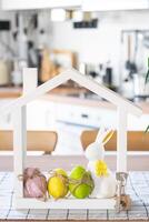 Key and tiny house of cozy home with Easter decor with rabbit and eggs on table of kitchen. Building, design, project, moving to new house, mortgage, insurance, rent and purchase real estate photo