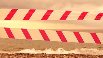 rood wit waarschuwing plakband barrière lint swinging in de wind aan de overkant exotisch zee strand achtergrond zonder mensen. Nee binnenkomst rood wit voorzichtigheid plakband. Nee vakantie concept, vertraagd reis, Nee zomer plannen video