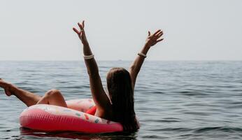 mujer verano mar. contento mujer nadando con inflable rosquilla en el playa en verano soleado día, rodeado por volcánico montañas. verano vacaciones concepto. foto