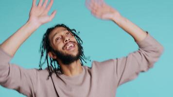 Ecstatic middle eastern person having fun, throwing hands in air, celebrating, enjoying leisure time. Joyful BIPOC man entertaining himself doing upbeat gesturing, studio background, camera B video