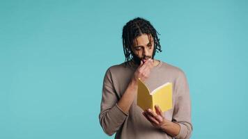 medio oriental hombre leyendo recién liberado de tapa dura libro desde editor, entretenido por fascinante historia. bipoc persona disfrutando literatura novela durante ocio hora en estudio fondo, cámara un video