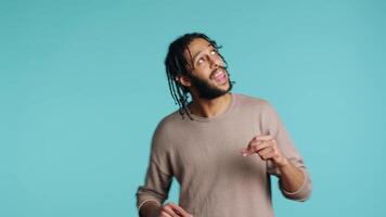 contento mezzo orientale ballerino avendo divertimento, danza su ritmo, godendo tempo libero volta. allegro bipoc uomo divertente lui stesso fare impaurito movimenti su musica, studio sfondo, telecamera un' video