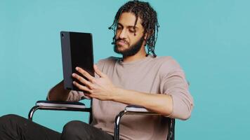 Artist in wheelchair holding tablet, using tactile touchscreen to draw. Person with disability doing digital art on drawing portable device, enjoying hobby in studio background, camera B video