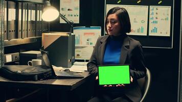 Private detective using tablet showing greenscreen template in incident room, working with witness statements and classified records. Agent holding device with isolated mockup. Camera A. video
