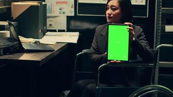 Detective wheelchair user holds greenscreen layout on tablet, using copyspace isolated display on gadget in incident room. Private investigator holding device with mockup screen. Camera A. video