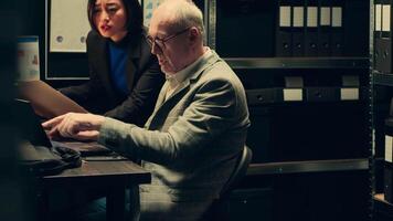 Private detectives reviewing forensic evidence folders in police archive room, collaborating on creating a profile for culprit. Team members studying old case files to connect the dots. Camera A. video