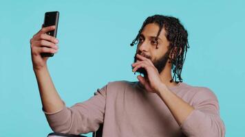 Man in wheelchair saluting friend over online videocall on cellphone, enjoying leisure time. Smiling person with disability bonding with mate using phone videoconference, studio background, camera B video