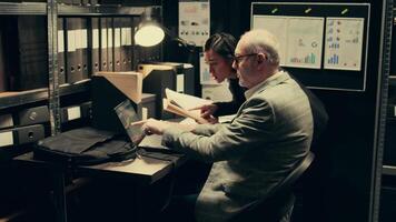 Law officers reading confidential folders in archive room at private company, gathering information to conduct investigation. Detectives create timelines based on archived records. Camera B. video