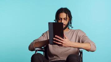 persona con paraplegia utilizzando tavoletta per inviare immagini su sociale media, fare autoscatto e scrittura foto didascalia. uomo nel sedia a rotelle utilizzando in linea la modifica applicazione su digitale dispositivo, studio, telecamera un' video