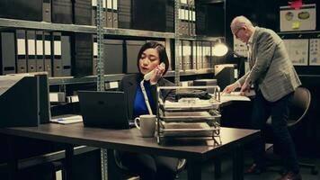 Law officer verifying details for the private investigation, working in archive room. Detective cross checks information on landline phone call, contacting people from records. Camera B. video