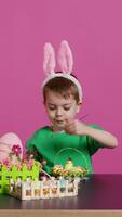 content petit enfant organiser des œufs et poussin dans une panier dans préparation pour Pâques dimanche célébrations, création de fête décorations dans studio. peu garçon ayant amusement coloration. caméra b. video