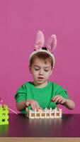 contento lieta bambino decorazione Pasqua accordi con fatto a mano Oggetti, organizzazione dipinto colorato uova nel un' cestino. gioioso poco ragazzo festeggiare primavera festa, rosa sfondo. telecamera b. video