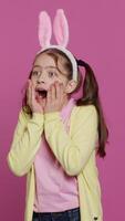 Vertical Video Adorable surprised schoolgirl being in shock after seeing something in studio, smiling and feeling very happy. Joyful small child with bunny ears being amazed by gifts. Camera A.