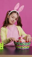 Excited young girl arranging painted eggs in a basket to prepare for easter holiday celebration, creating festive arrangements. Playful happy toddler with bunny ears, creative activity. Camera B. video