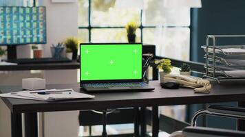 Wheelchair in office offering accessibility to workers with disability and green screen laptop on desk. Mockup notebook in workspace and computer screen in background displaying stock exchange video