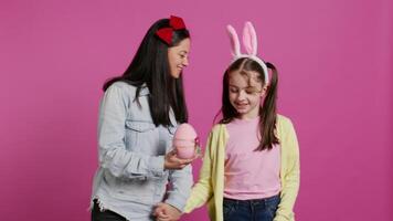 Cute mother and daughter dancing around in the studio, having fun together and doing dance moves on groovy music. Mom giving a big easter egg to her kid, carefree confident little family. Camera B. video