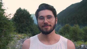 A young handsome brunette with glasses smiles at the camera in nature video