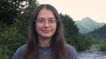 young beautiful brunette with glasses smiles at the camera in nature video