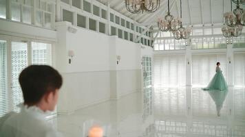 Elegant woman in a flowing dress walking in a luxurious, bright room with chandeliers, observed by a man holding a candle. video