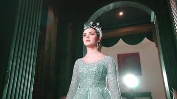 elegante mujer en un espumoso vestir y tiara posando en un lujoso habitación con dramático Encendiendo. video