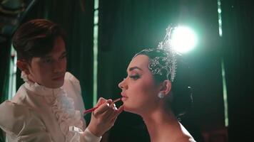 Makeup artist applying lipstick to a model with elegant headpiece in a backstage setting. video