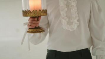 Person in elegant attire holding a candle lamp, with focus on the ruffled shirt and vintage lamp. video