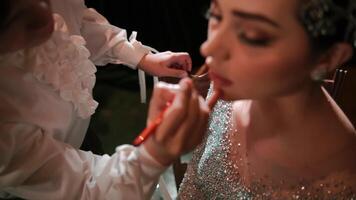 Makeup artist applying lipstick to a model in elegant attire with a tiara, backstage preparation concept. video