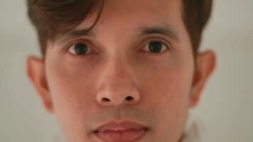 Close-up portrait of a young man with a neutral expression on a plain background. video