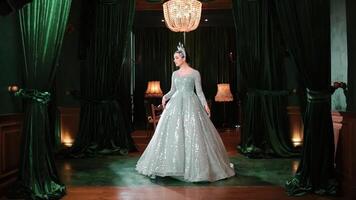 Elegant woman in a sparkling gown standing under a chandelier in a luxurious ballroom setting. video
