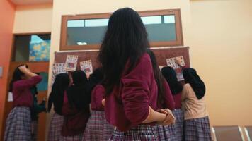 posterior ver de colegialas en uniformes mirando a boletín tablero en un salón de clases ajuste. video