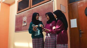 Tres joven mujer en hijabs sonriente y mirando a un teléfono inteligente juntos adentro. video