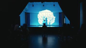 silhueta do uma pessoa em etapa com uma vibrante azul luz projeção dentro a fundo, público dentro a primeiro plano. video