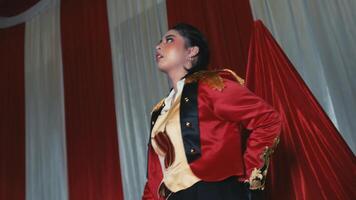 confidente joven mujer en un graduación vestido y gorra en pie en frente de un rojo cortina. video