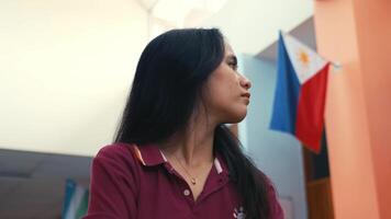 Profile of a young woman in a classroom with a Philippine flag in the background. video