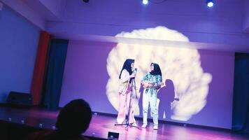 Two women with hijabs presenting at a conference, one speaking into a microphone. video