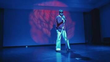 Performer singing on stage with dramatic blue lighting and red abstract backdrop. video
