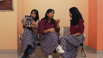 Tres joven mujer en colegio uniformes sentado y charlando, uno participación un libro. video