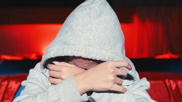 Person in gray hoodie covering face with hands, conveying emotion of sadness or distress, with a red background. video