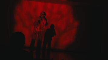 Singer performing on stage with red spotlight and shadow silhouette video