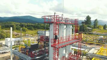 Aerial view gas station operator descends from the top of the station. Modern gas complex in the mountains. A gas worker climbs the ladder of the gas distribution unit, against the backdrop of video