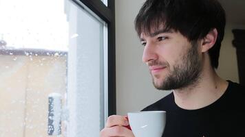 un hombre disfruta el aroma de Mañana café por el ventana en invierno. video