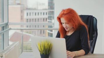 Young successful woman happily smiling at workplace working with laptop. The case was successfully completed. Woman relaxes after sending a message over the Internet. video