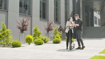 Young man and woman businesspeople talking and smiling with smartphone in hands on the street in industrial town. Woman with a yellow folder and an electric scooter video