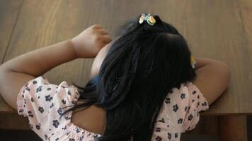 uma pequeno menina é sentado às uma mesa com dela cabeça em repouso em dela mãos video