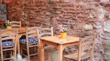 all'aperto legno duro tavolo e sedie contro un' mattone parete, con un' vaso di fiori su superiore video