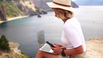 digital nômade, o negócio mulher trabalhando em computador portátil de a mar. bonita senhora digitando em computador de a mar às pôr do sol, faz uma o negócio transação conectados a partir de uma distância. freelance, controlo remoto trabalhos em período de férias video