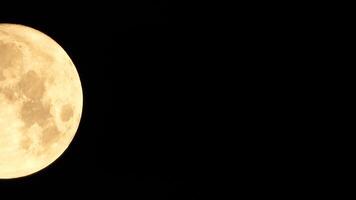 A glowing golden huge full moon seen from earth through the atmosphere against a starry night sky. A large full moon moves across the sky, the moon moving from the left frame to the right. video