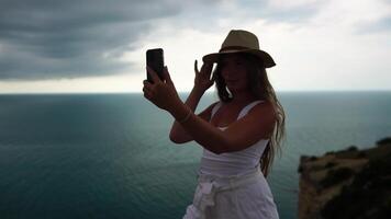 kvinna resa hav. Lycklig turist i hatt njut av tar bild utomhus för minnen. kvinna resande Framställ på de strand på hav omgiven förbi vulkanisk berg, delning resa äventyr resa video